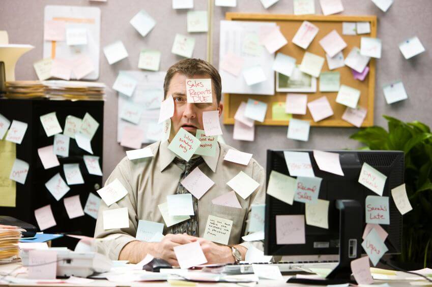 Patchwork of Spreadsheets Unviable for Client Loads in the Thousands 1 Overwhelmed man at desk covered in sticky notes illustrating inefficient client management processes.