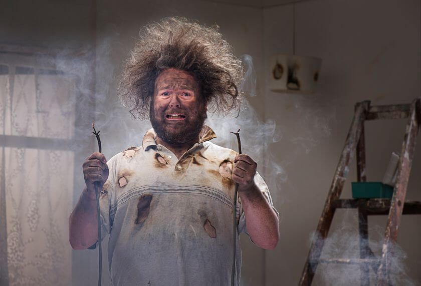 Hiring a Custom Application Developer: The Four Rules to Avoid Disaster 1 Man with shocked expression holding damaged electrical wires, illustrating potential disaster in custom application development.